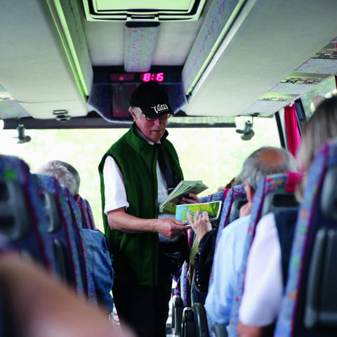 Rejseleder, der deler brochurer ud til gæster ombord på en bus fra Vitus Rejser.
